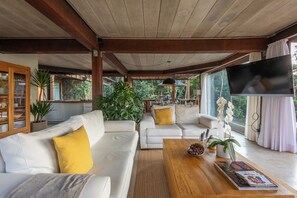 Un'ampia zona living con un divano bianco, un tavolino da caffè e un televisore. Si vedono piante e una libreria nella stanza.