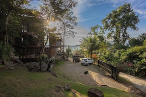A gravel driveway leading to a wooden house with a car parked nearby. - Residencial Cambaquara 4 (Ilhabela)