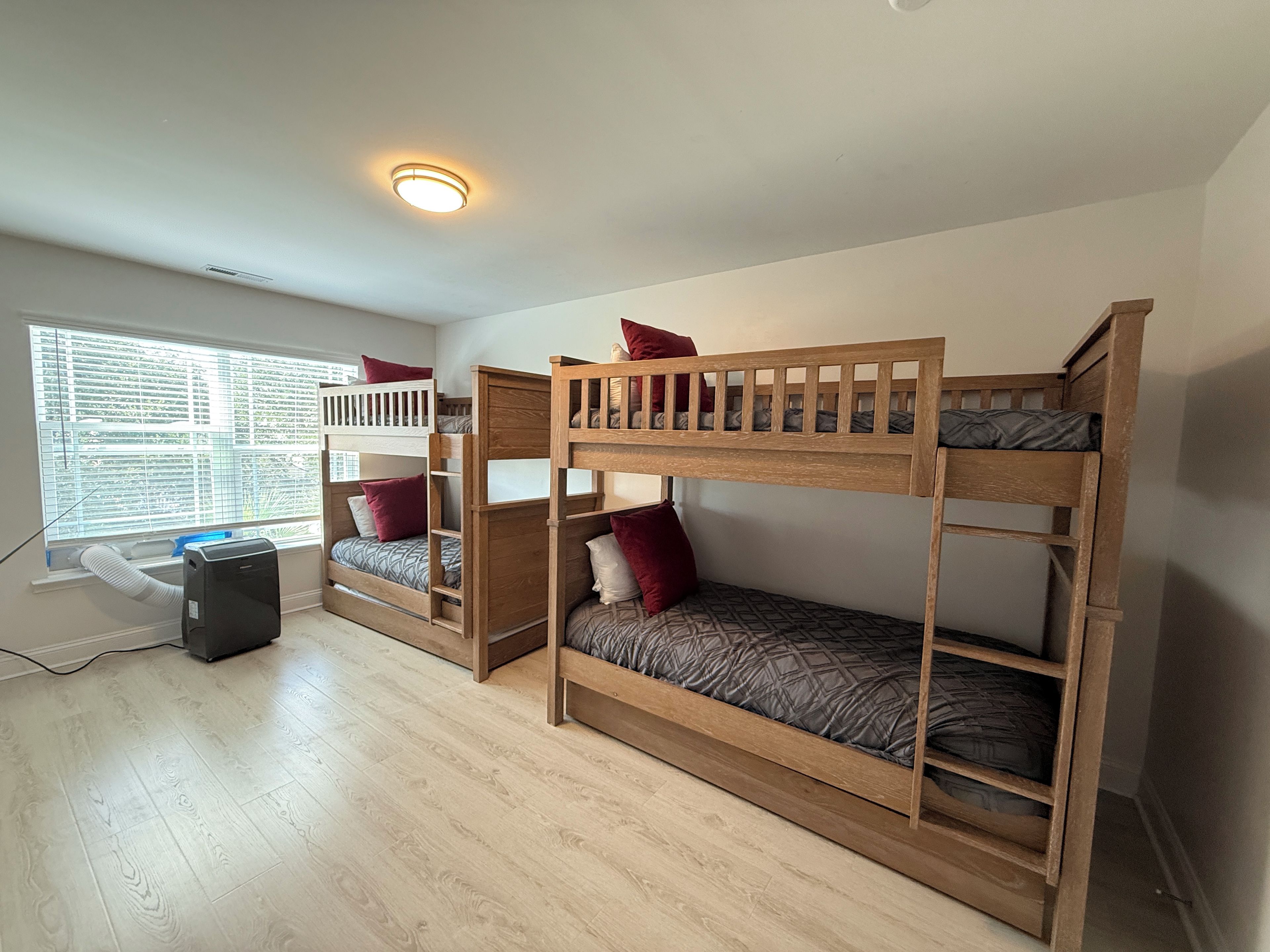 Une chambre avec deux lits superposés, une fenêtre avec des stores, un bureau et un luminaire au plafond.