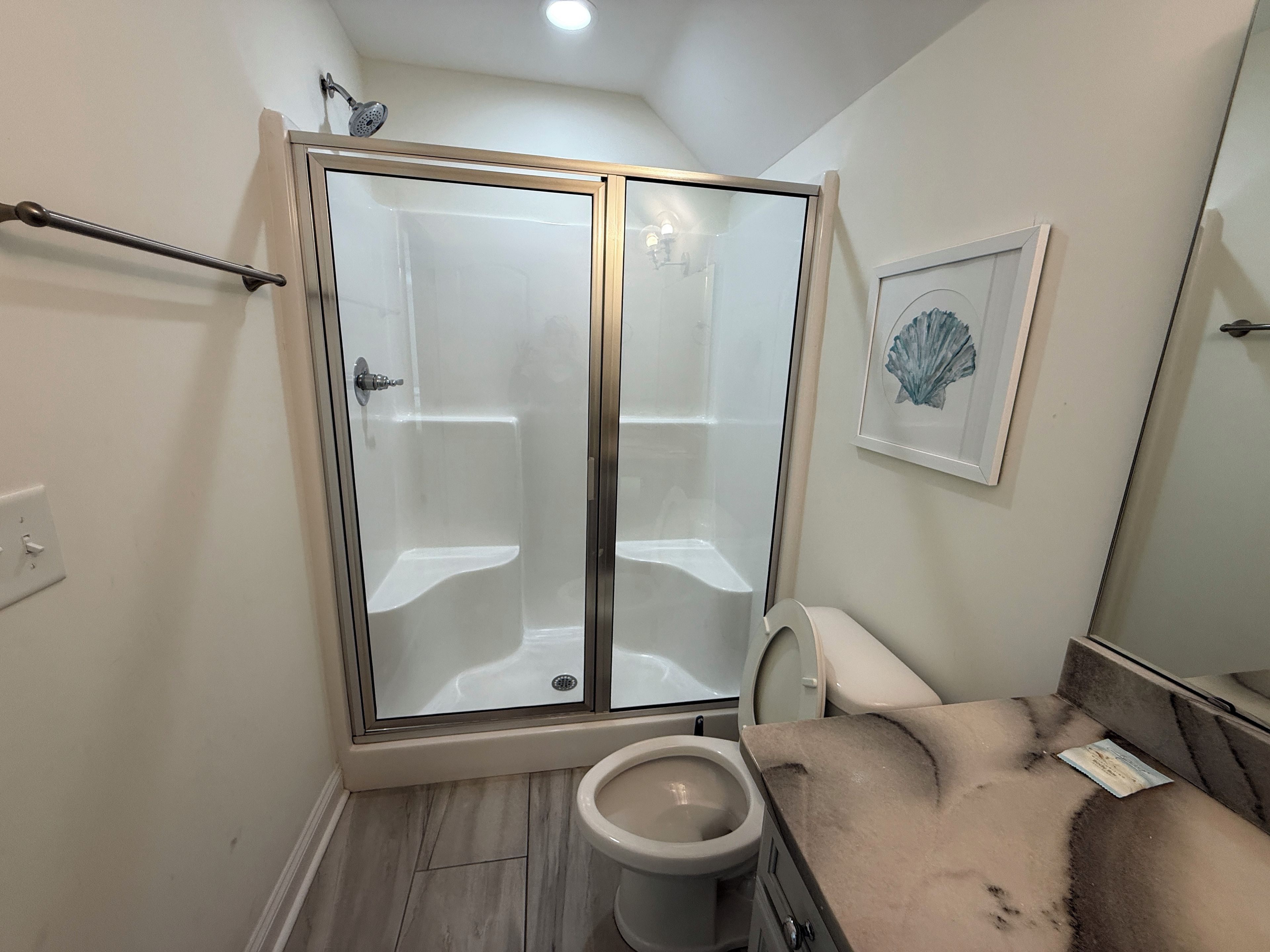 Ein Badezimmer mit einer gläsernen Duschkabine, einer Toilette und einem Waschtisch mit Marmorplatte.
