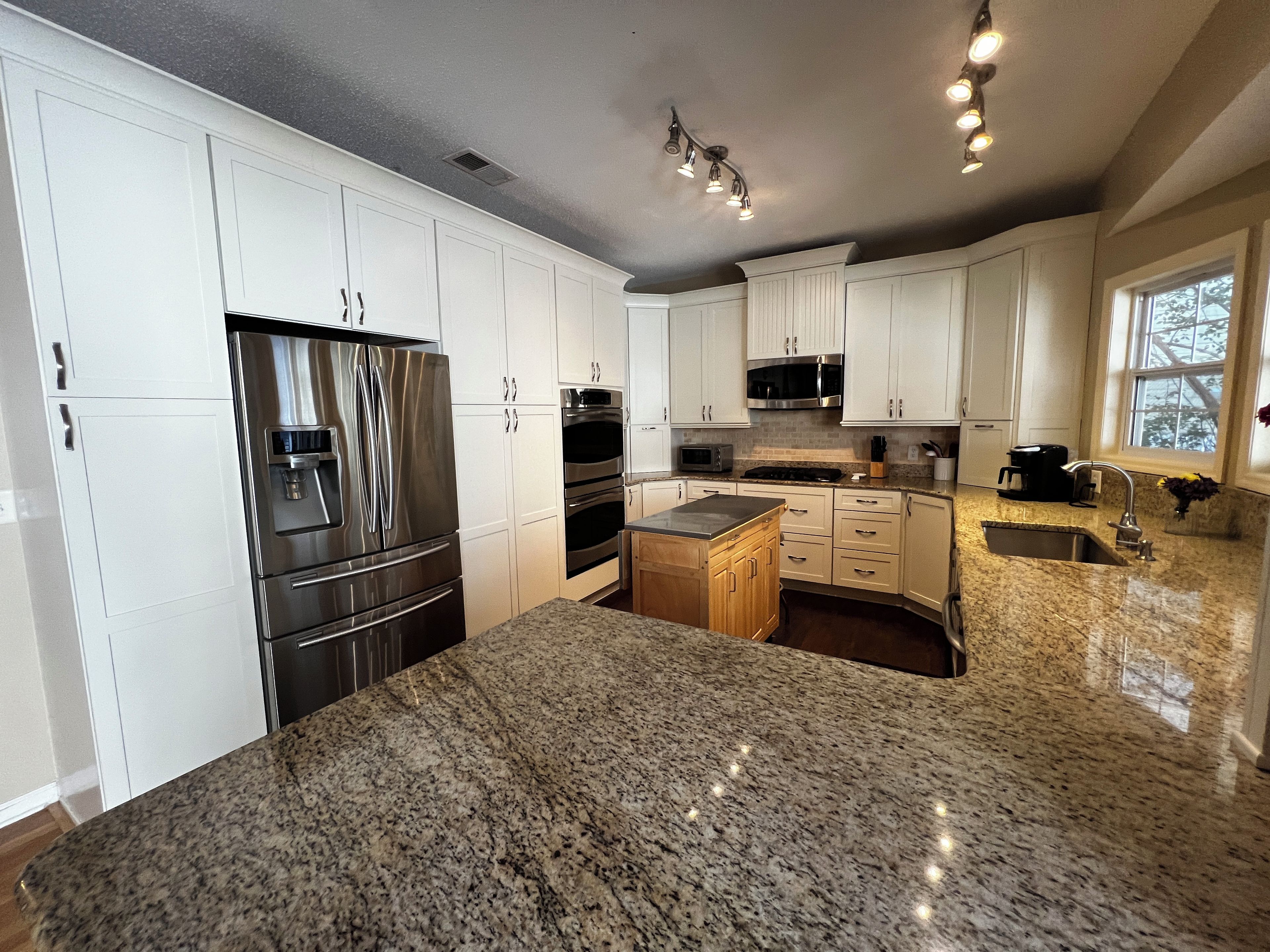 A kitchen with white cabinets, stainless steel appliances, granite countertops, and a window providing natural light.