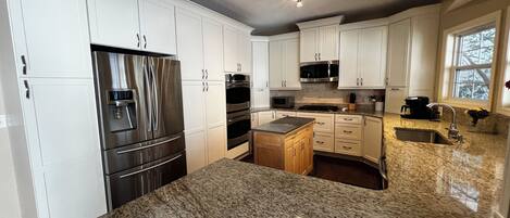 A kitchen with white cabinets, stainless steel appliances, granite countertops, and a window providing natural light.