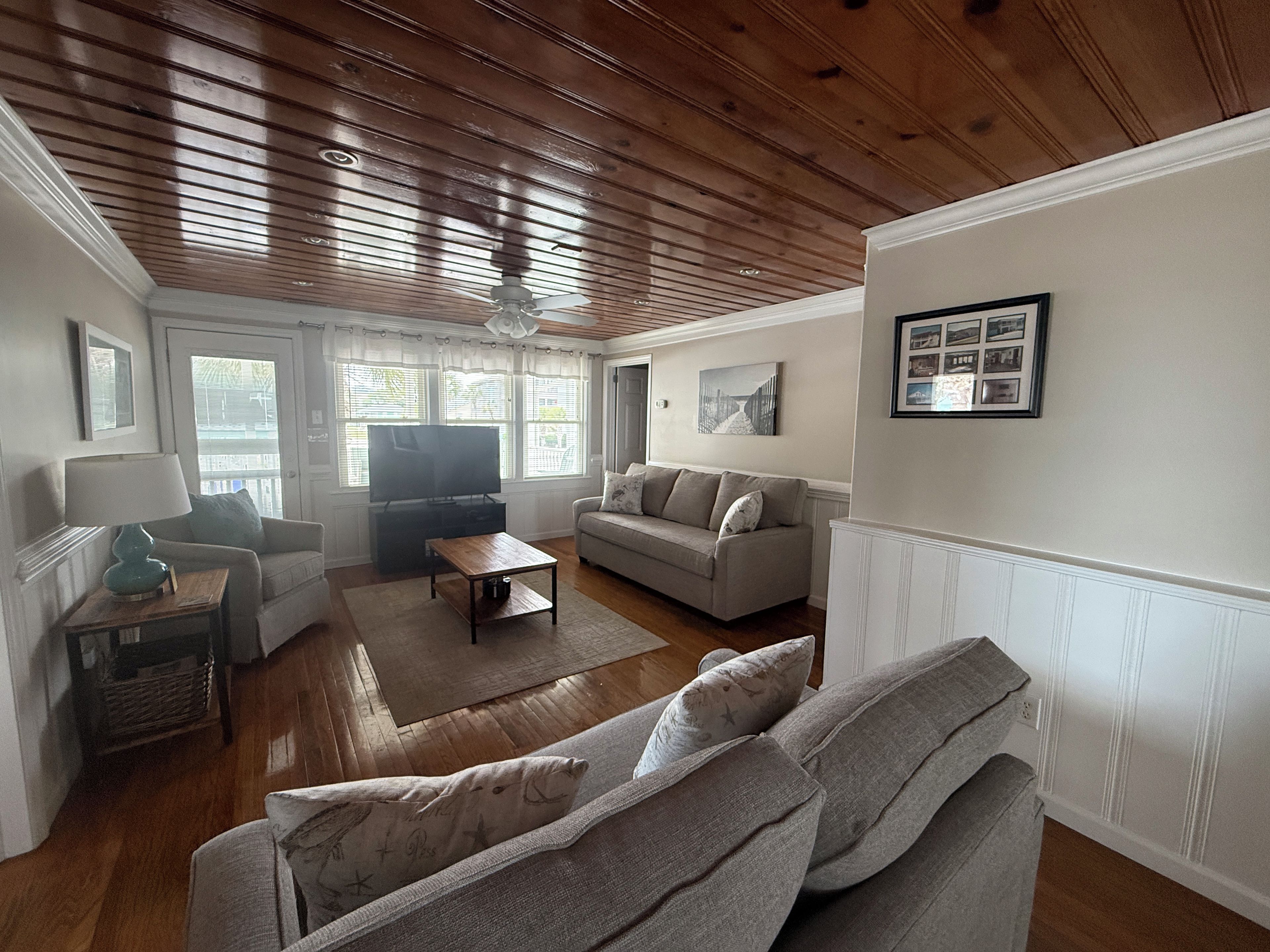 Een woonkamer met een houten plafond, een televisie, een bank, een salontafel en een lamp.