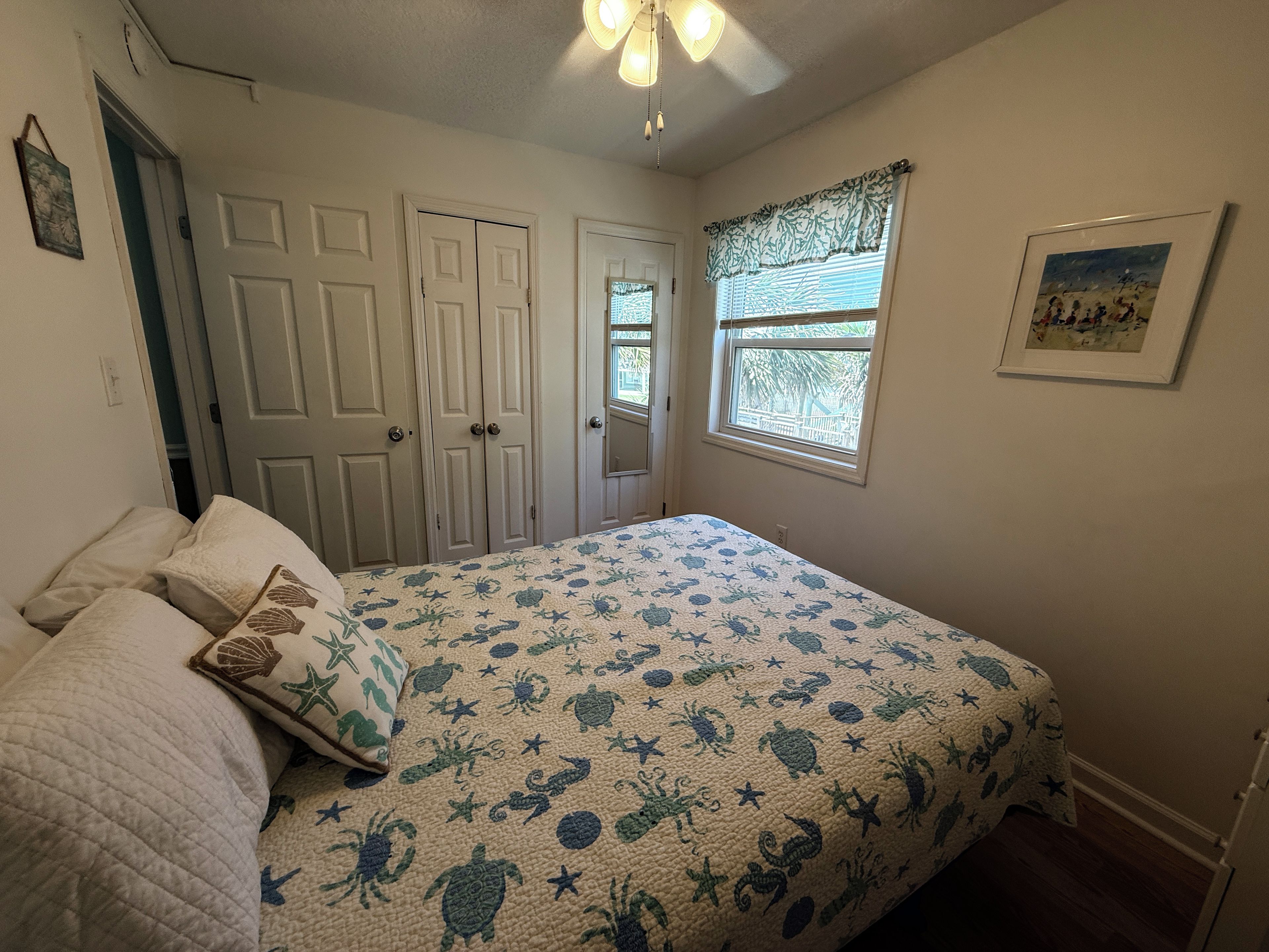 A bedroom with a bed, a window with blinds, a door, and a ceiling fan.