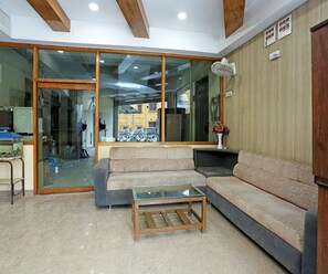 A modern interior with a glass door leading to a parking area, a sofa, a coffee table, and a fan on the wall. - Deluxe Room Hotel Natraj (Raipur)