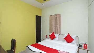 A hotel room with a bed, a desk, a chair, a ceiling fan, and a nightstand with a phone.
