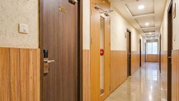 A hotel corridor with wooden doors, a fire alarm, and a light switch on the wall.