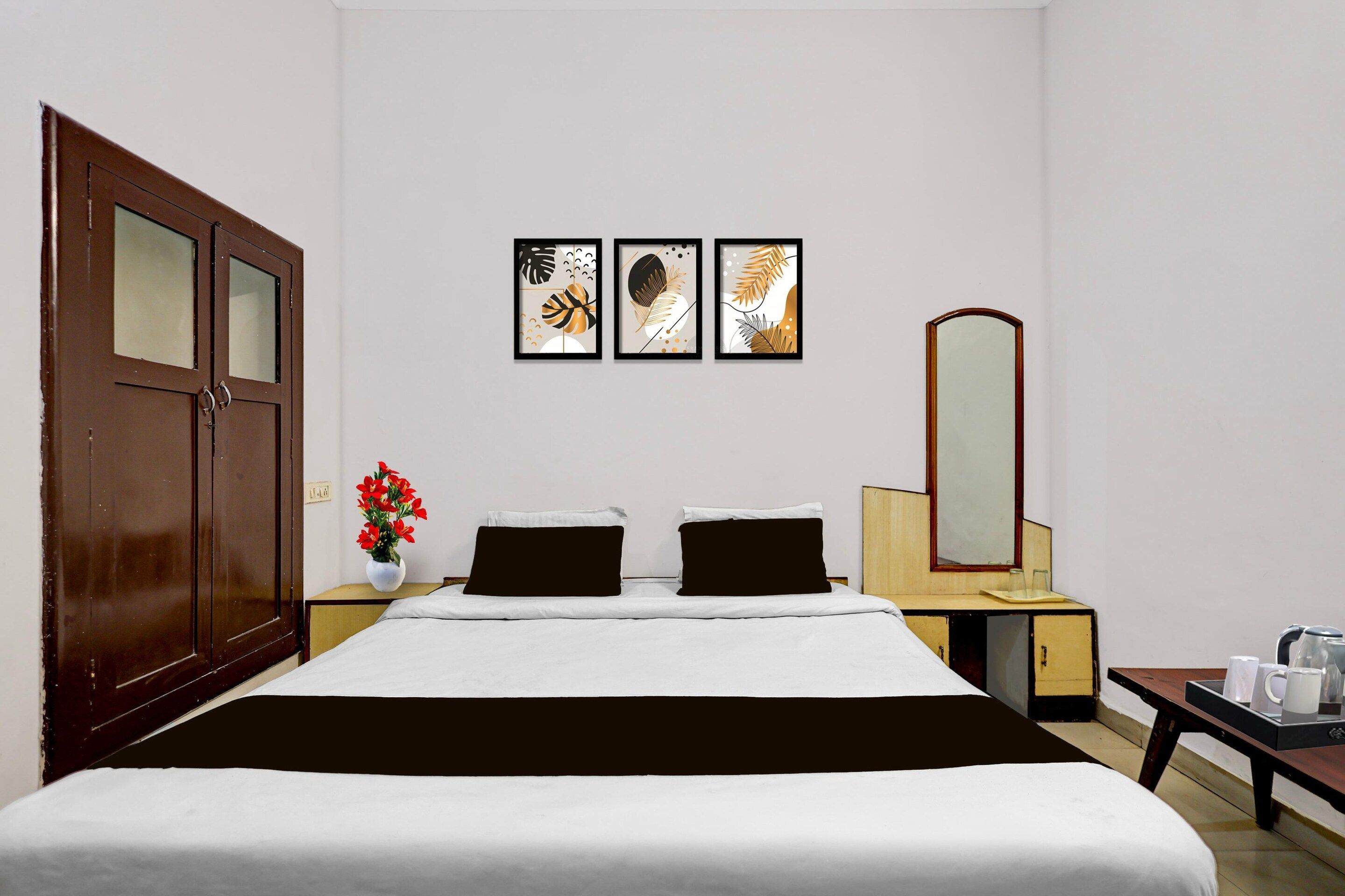 A hotel room with a bed, a nightstand, a dresser, a mirror, and three framed artworks on the wall.