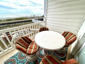 Ein Balkon mit rundem Tisch und vier Stühlen, der Blick auf einen Strand geht.