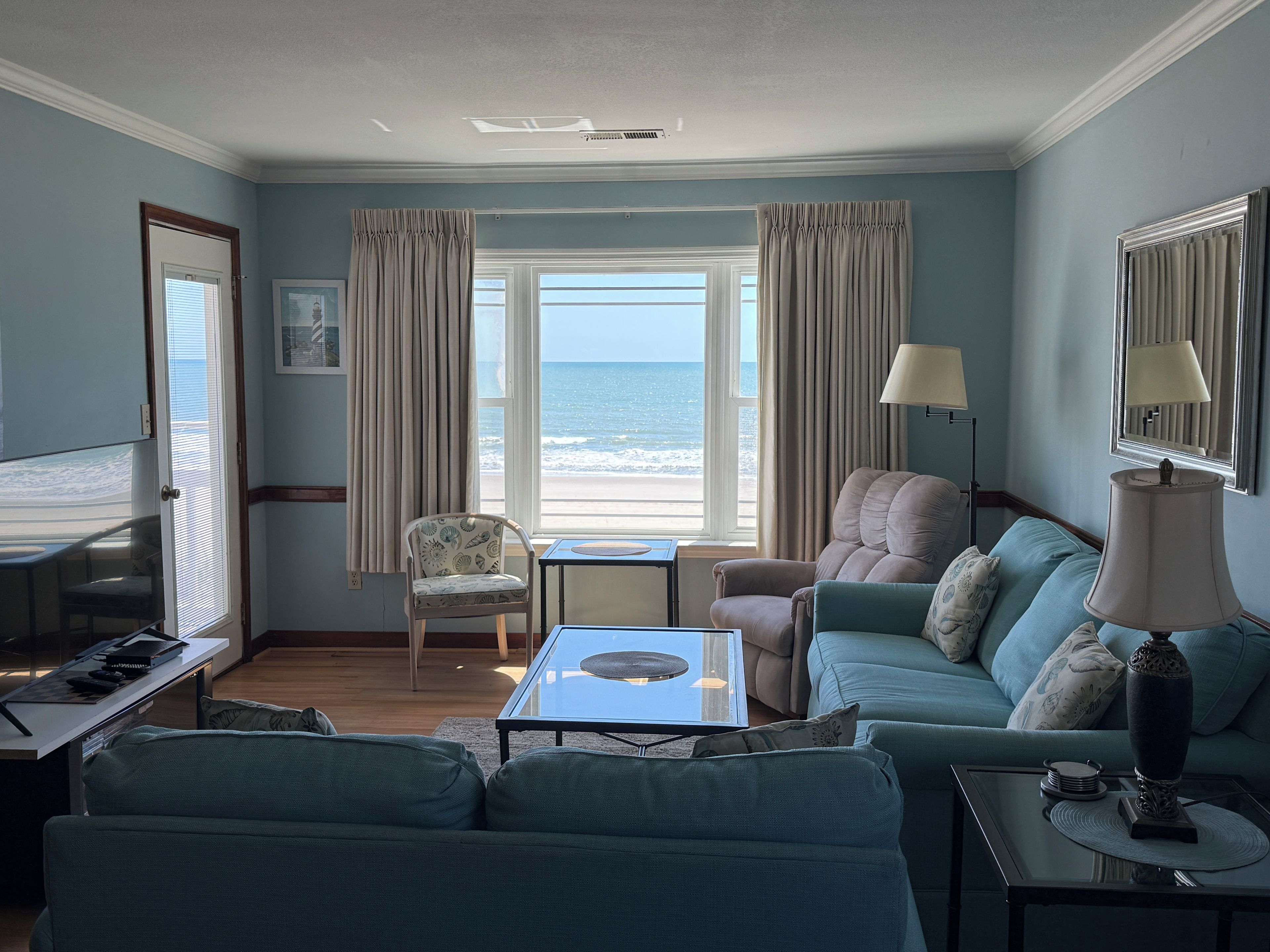 A living room with a view of the ocean, a sofa, a chair, a table, and a lamp.