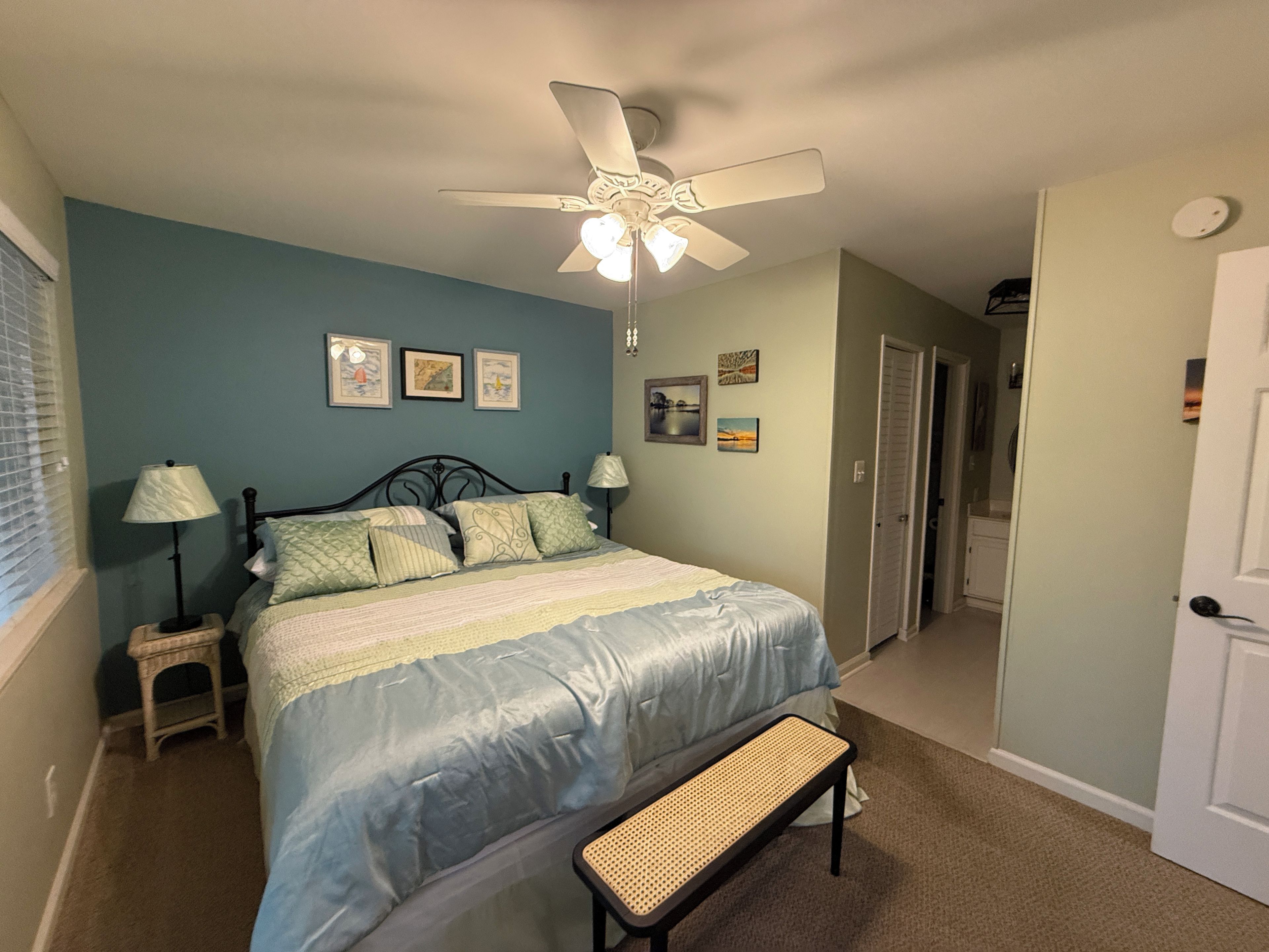 A bedroom with a bed, a ceiling fan, a bench, and a door leading to another room.