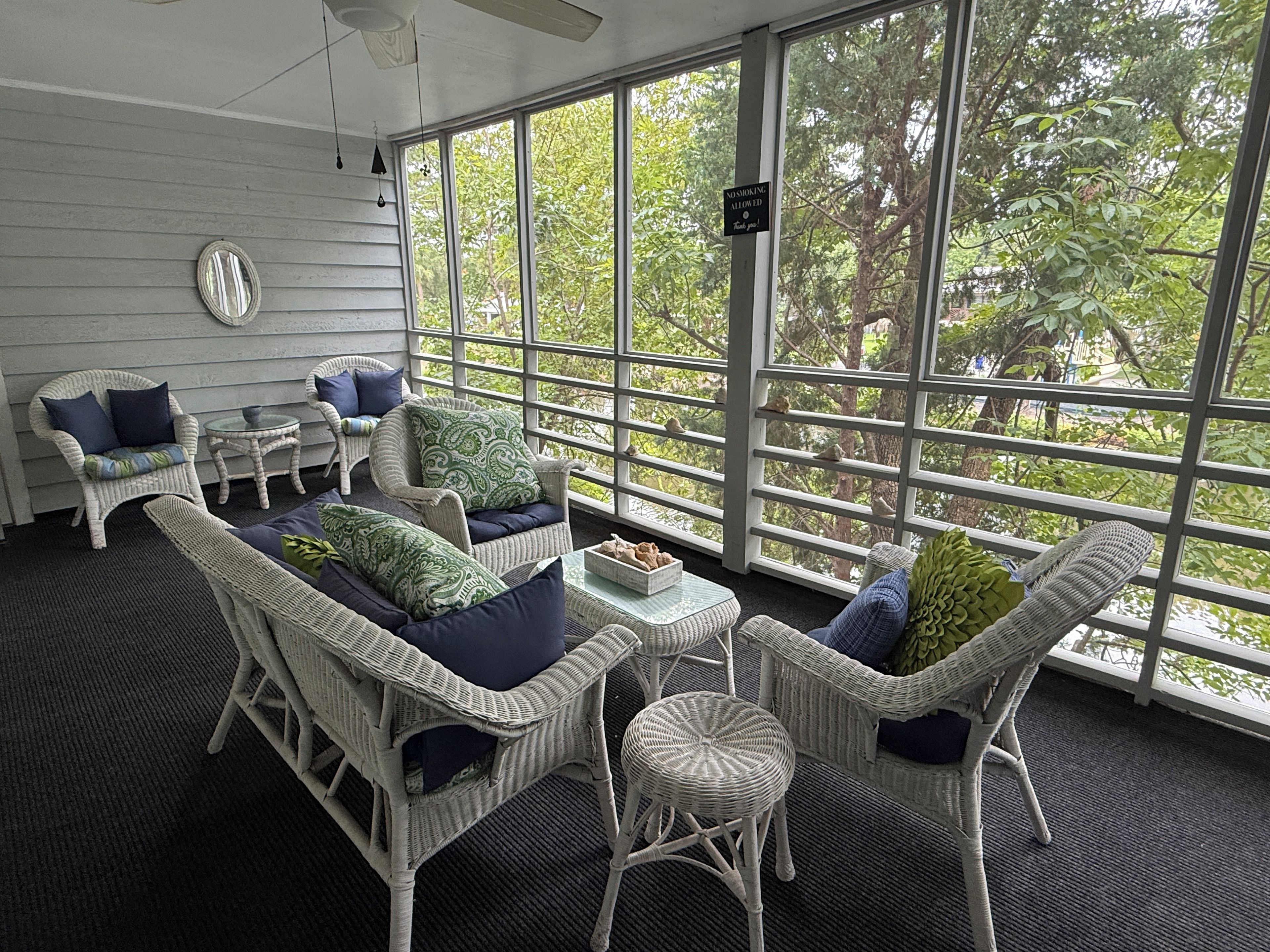 A sunlit room with wicker furniture, large windows, and a ceiling fan.