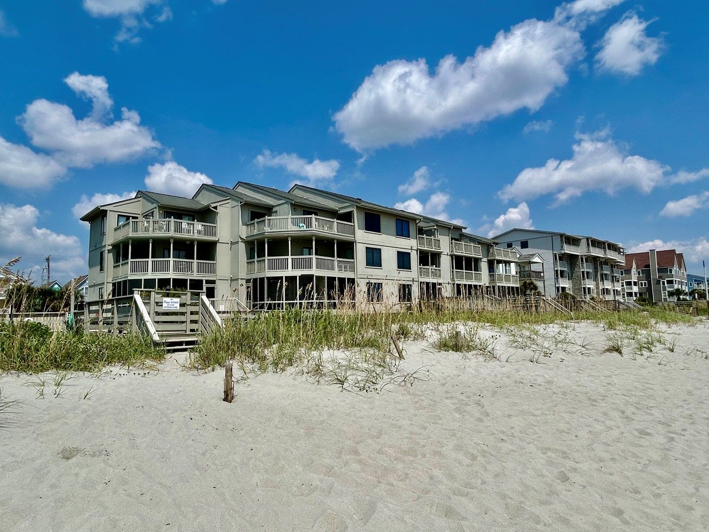 A beachfront hotel with multiple balconies, a sandy beach in the foreground, and a clear blue sky.
