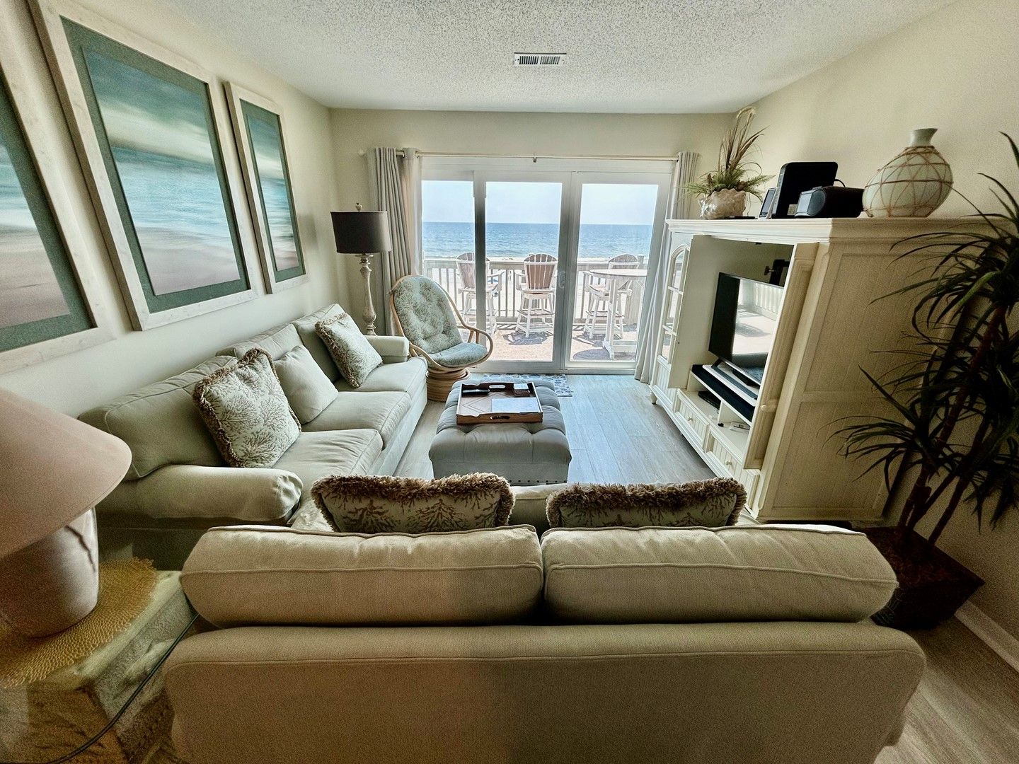 A living room with a sofa, armchairs, a coffee table, a TV, and a view of the sea through large windows.