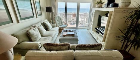 A living room with a sofa, armchairs, a coffee table, a TV, and a view of the sea through large windows.
