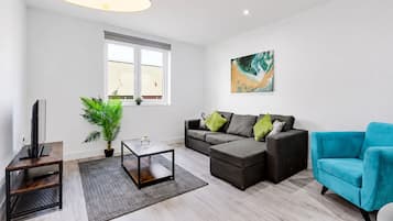 A modern living room with a sofa, a coffee table, a TV, and a plant.