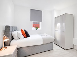 A modern bedroom with a bed, bedside lamp, wardrobe, and a window with a view of a building. - Contractor/CorporateTravel/Relocation, MyRent2Rent (Corby)