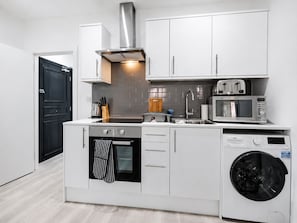 A modern kitchen with white cabinetry, a stainless steel range hood, a built-in oven, a microwave, and a front-loading washing machine. - Contractor/CorporateTravel/Relocation, MyRent2Rent (Corby)