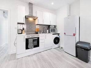 A modern kitchen with white cabinetry, a stainless steel range hood, a built-in oven, a microwave, a washing machine, and a refrigerator. - Contractor/CorporateTravel/Relocation, MyRent2Rent (Corby)