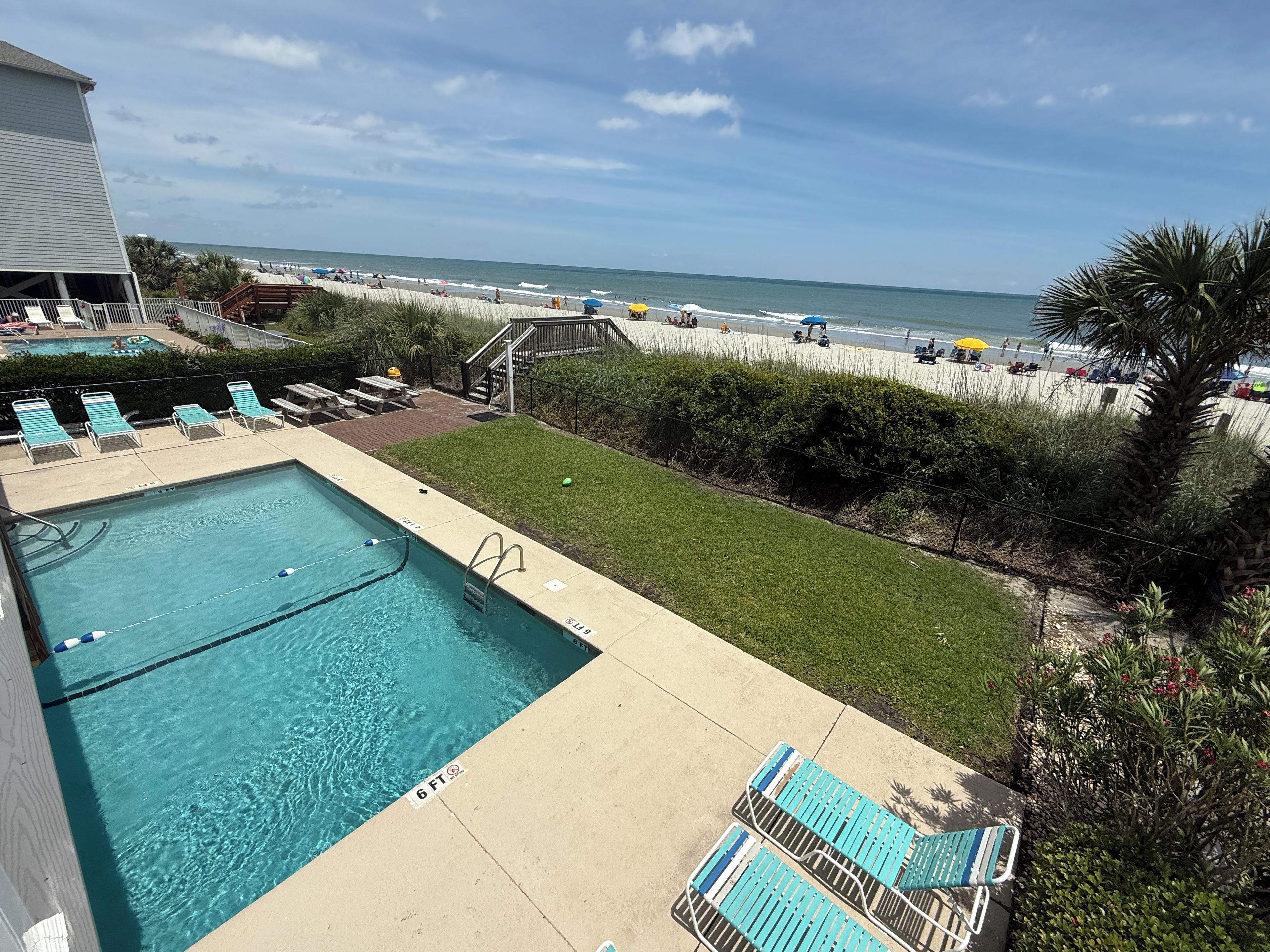 A pool area with lounge chairs, a diving board, and a view of the beach.