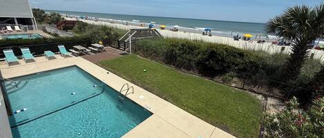 A pool area with lounge chairs, a diving board, and a view of the beach.