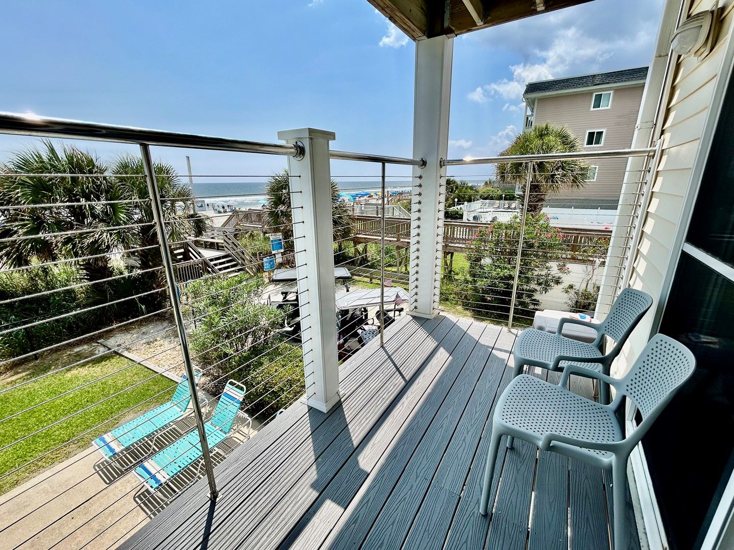 A balcony with a view of a beach and a pool, featuring a railing and a few chairs.