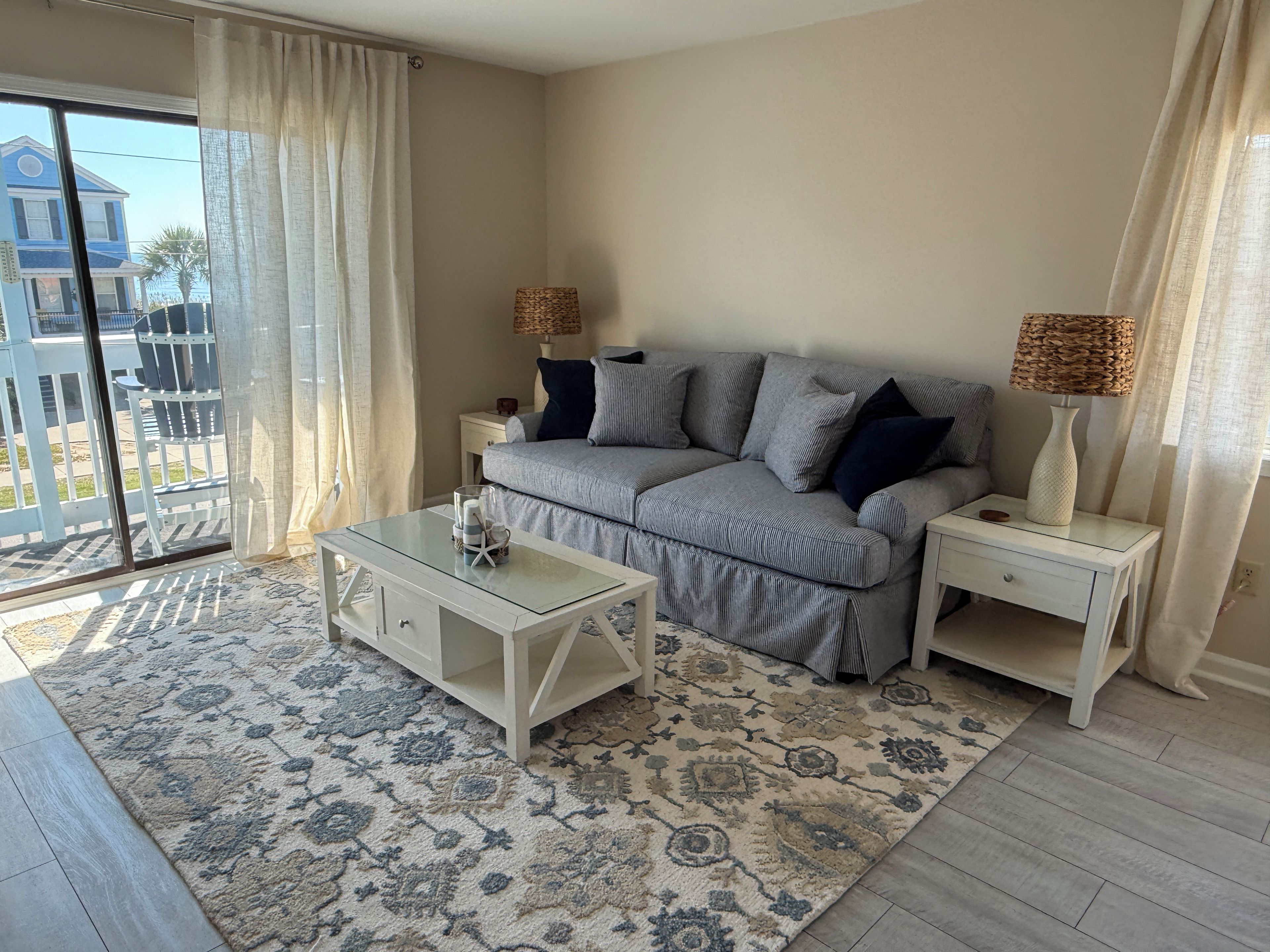 A living room with a sofa, two nightstands, a coffee table, and a view through a sliding glass door.