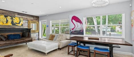 A modern living room with a sofa, a dining table with chairs, and artwork on the walls.