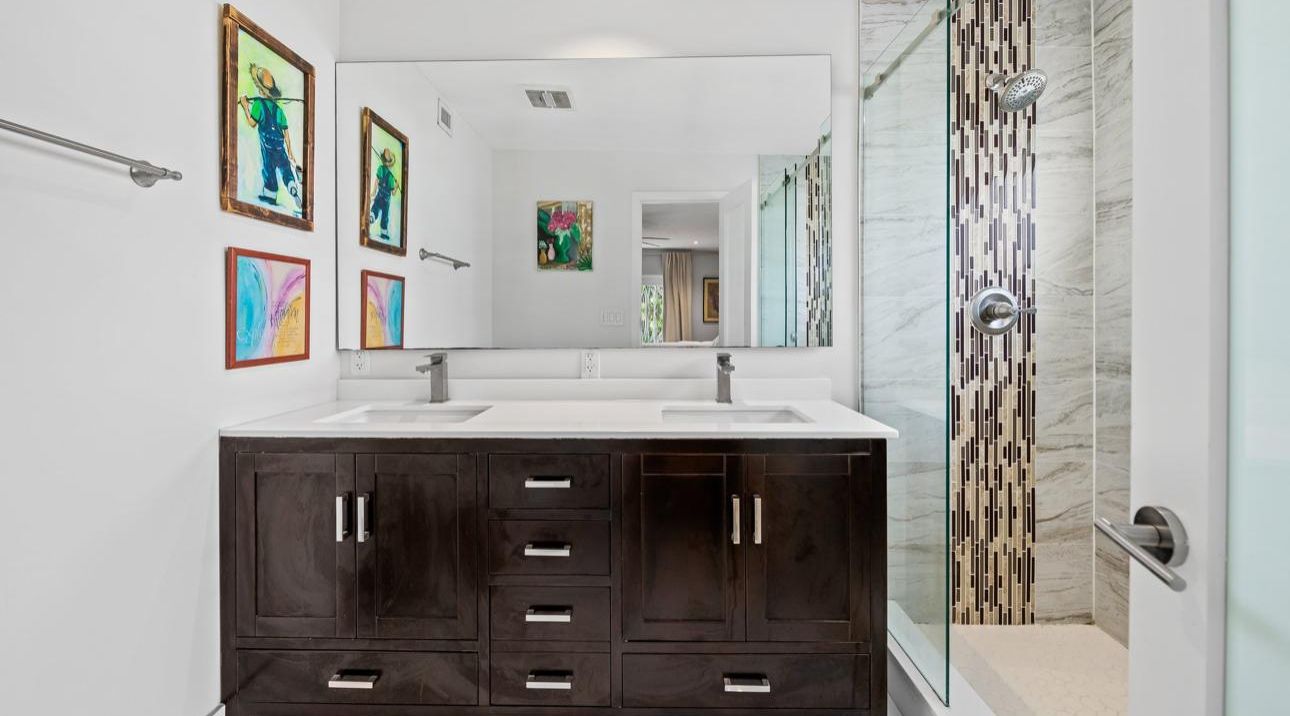 A modern bathroom with two sinks, dark cabinetry, and a shower area.