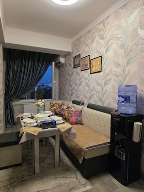 A living room with a dining area, a water dispenser, and a sofa with floral cushions.