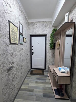 A hallway with a patterned wall, a white door, a wooden bench with a mirror, and a doormat.