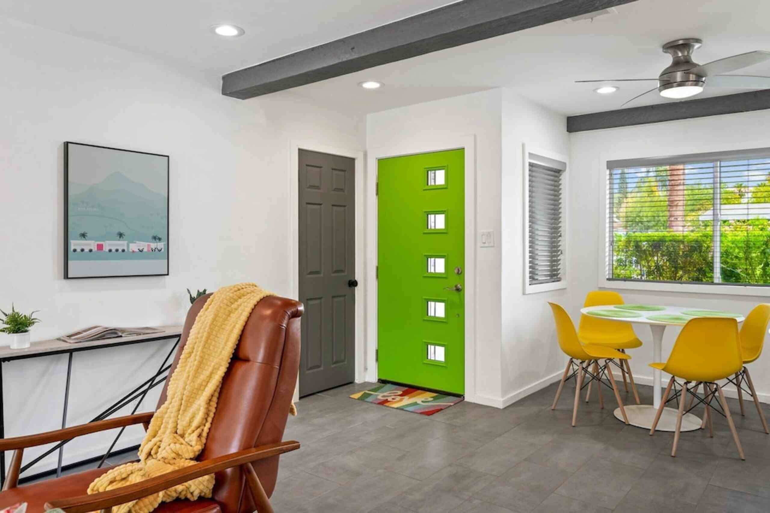 Una habitación moderna con comedor, una puerta verde y un ventilador de techo.