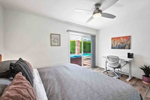 Ein Schlafzimmer mit Bett, Schreibtisch, Stuhl, Deckenventilator und Blick auf einen Pool.