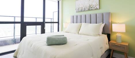 A bedroom with a large bed, a nightstand, a lamp, and a window with a view.