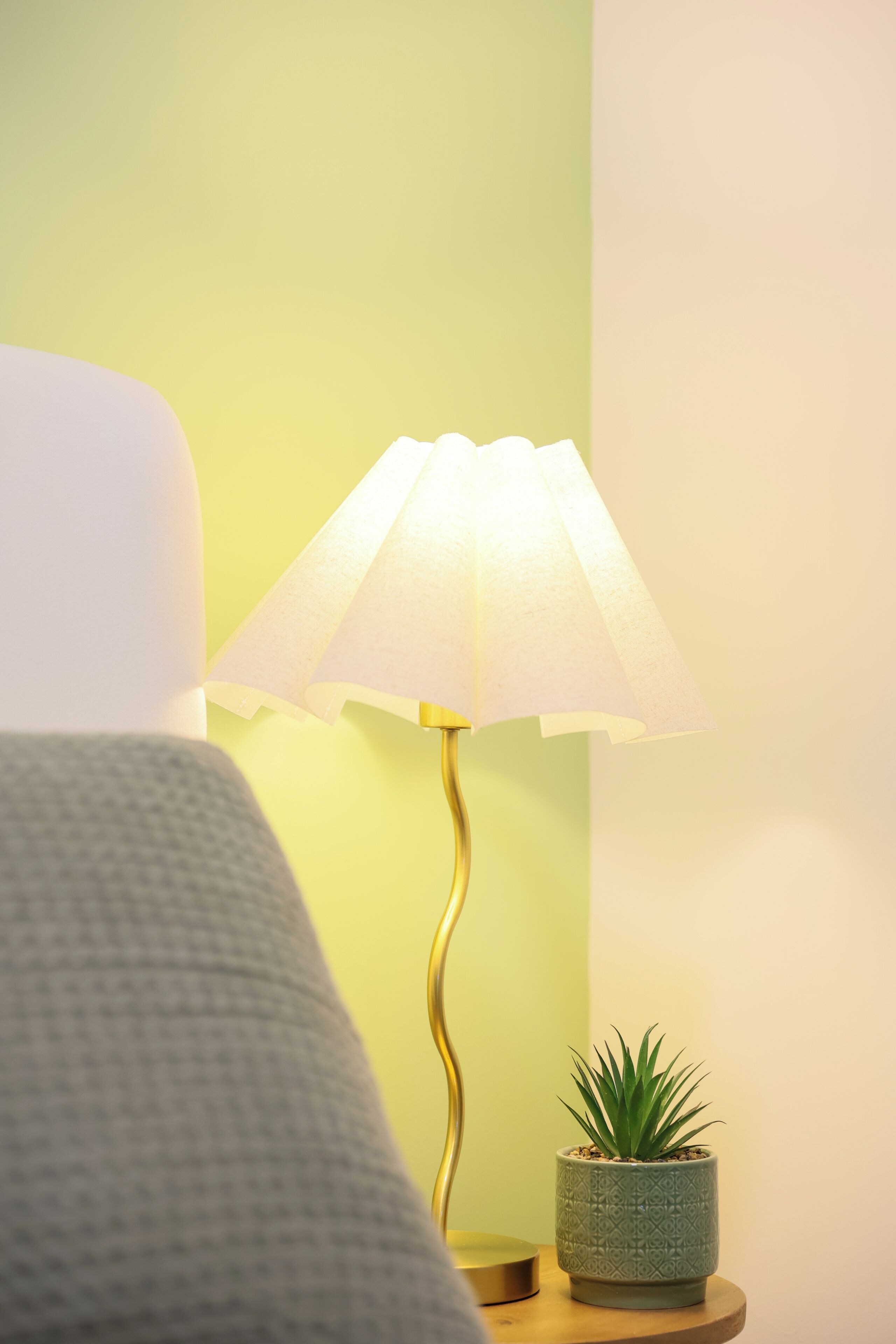 Une table de chevet avec une lampe, une petite plante en pot et un lit.
