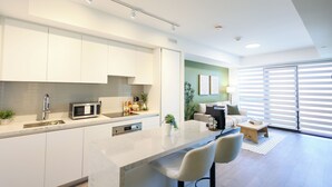 A modern kitchen with a built-in microwave, a coffee machine, and a bar area with bar stools. - Casa Verde | Skyline Views Near Square One (Mississauga)