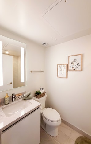 Un bany modern amb un lavabo blanc, un vàter i dues impressions enmarcades de motius florals a la paret.