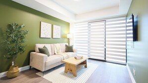A living room with a sofa, a coffee table, a lamp, a plant, and a sliding glass door with blinds. - Casa Verde | Skyline Views Near Square One (Mississauga)