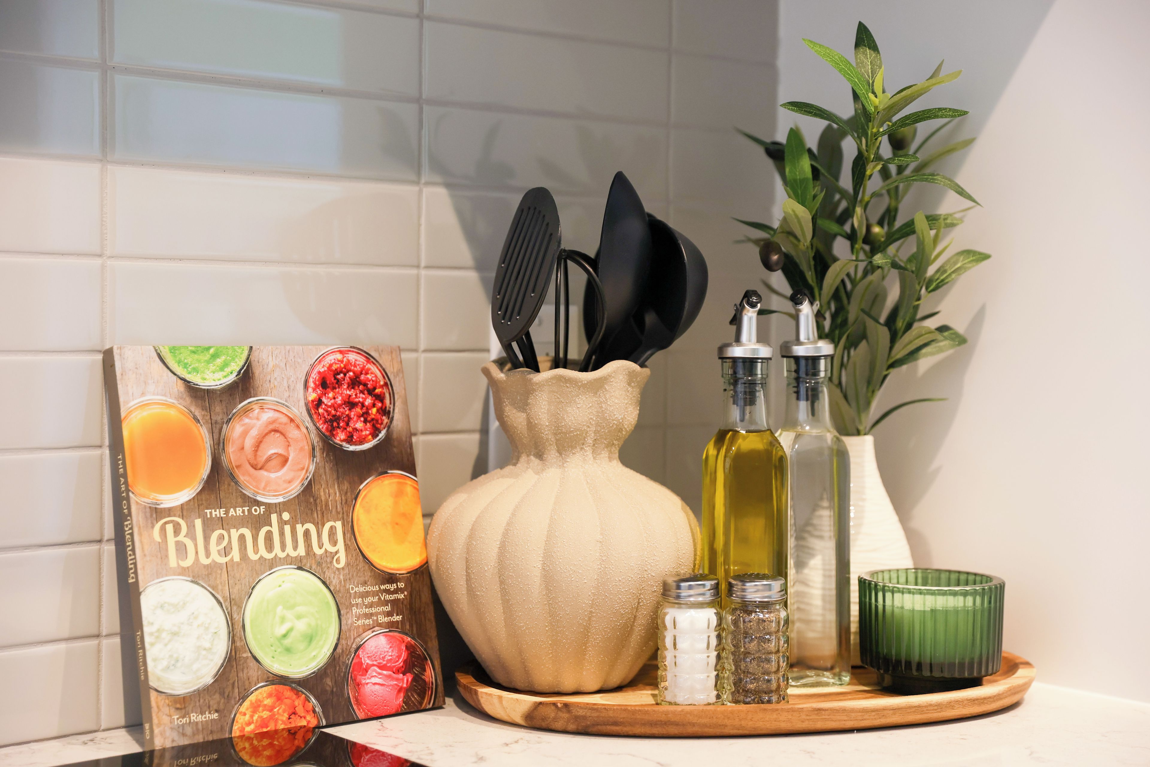 A kitchen counter with a blending book, a wooden pitcher, bottles, and a green candle.