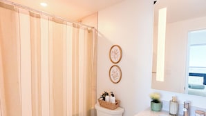 A bathroom with a toilet, a shower curtain, a sink, and a mirror. - Casa Verde | Skyline Views Near Square One (Mississauga)