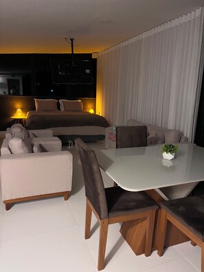 A modern hotel room with a bed, sofa, dining table, and a TV mounted on the wall. - Residencial canto dos passarinhos (Alto Paraíso de Goiás)