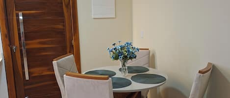 A dining area with a round table, four chairs, a vase with flowers, and a wooden door.