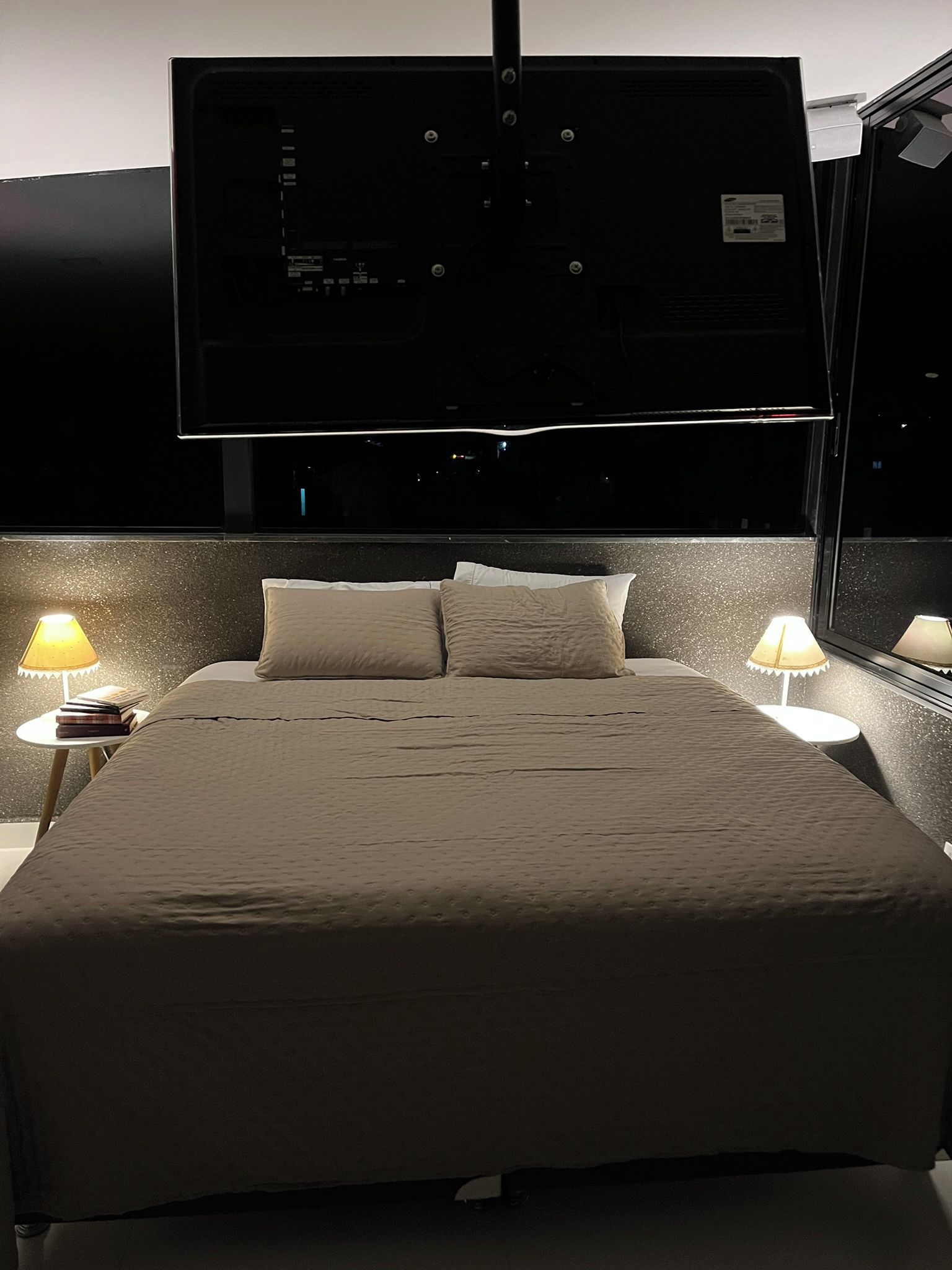 Habitación de hotel con cama, dos lámparas de noche, televisor de pantalla plana montado en la pared y una ventana.