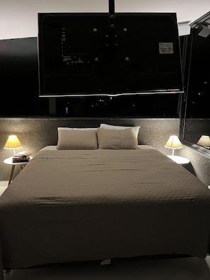 A hotel room with a bed, two bedside lamps, a flat-screen TV mounted on the wall, and a window. - Residencial canto dos passarinhos (Alto Paraíso de Goiás)