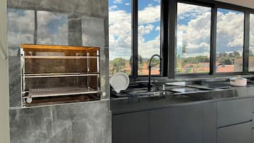 A modern kitchen with a built-in grill, a large window with a view of the sky and clouds, and a sink with a faucet.