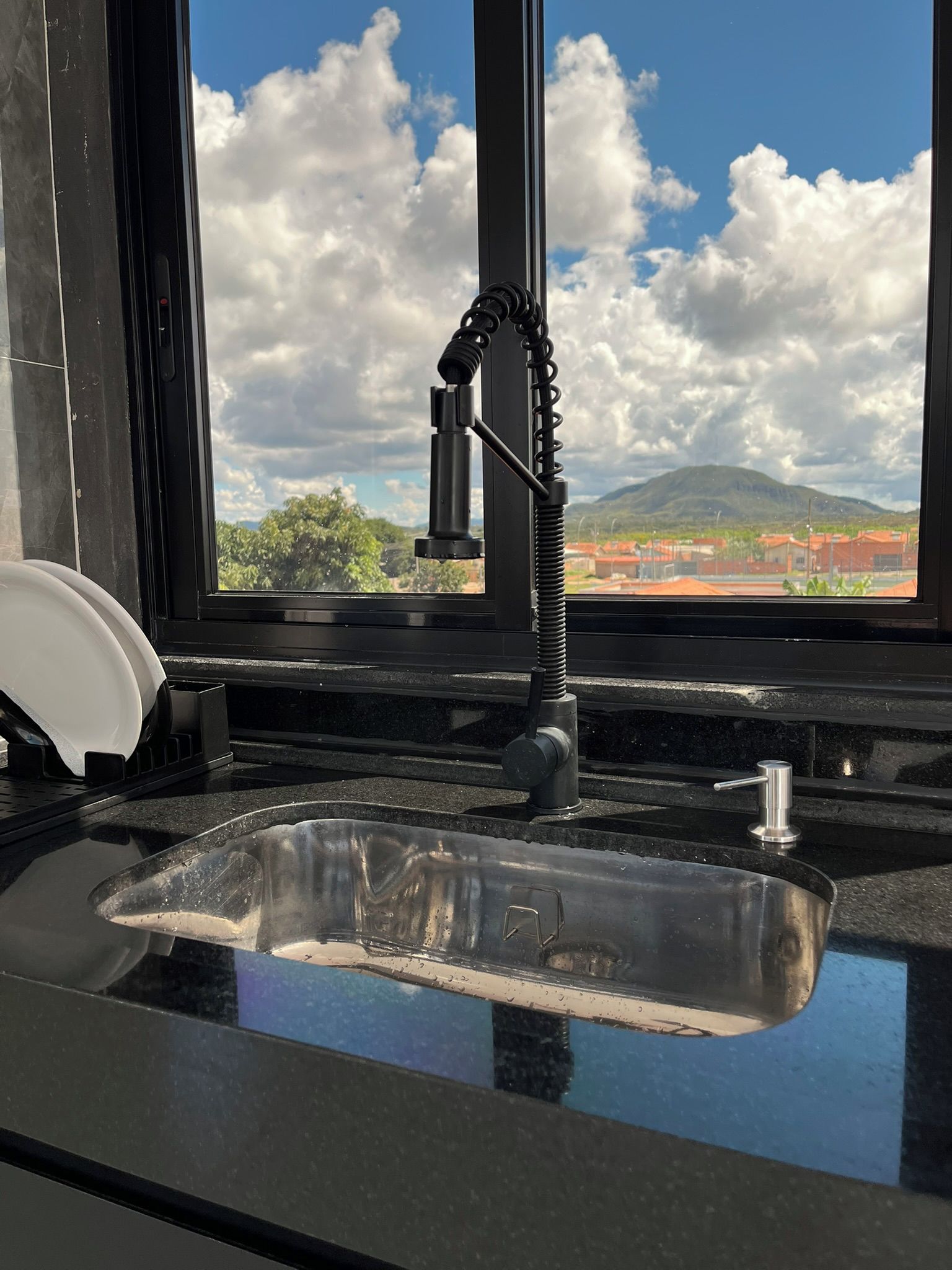 Eine Küche mit Spüle aus Edelstahl, einem Wasserhahn und einem Fenster mit Blick auf Berge und Wolken.
