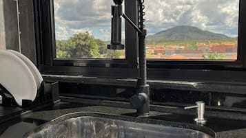 Eine Küche mit Spüle aus Edelstahl, einem Wasserhahn und einem Fenster mit Blick auf Berge und Wolken.