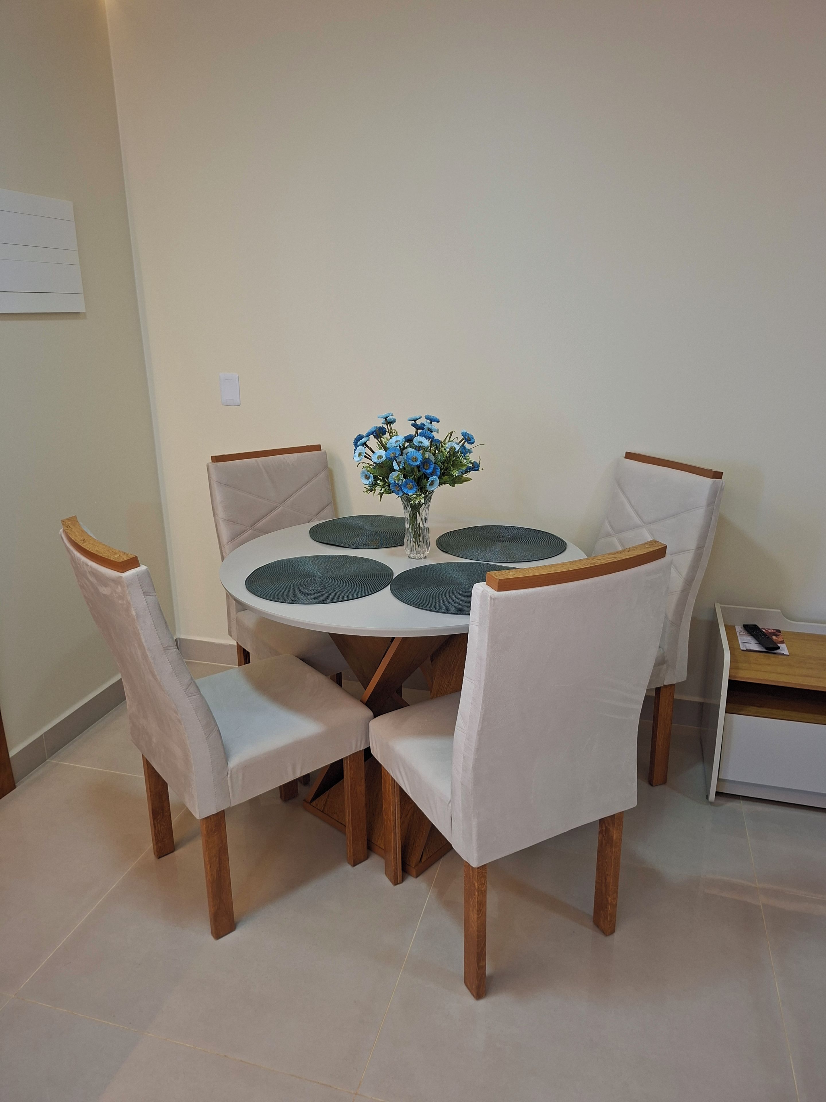 A dining area with a round table, four chairs, and a vase with blue flowers.