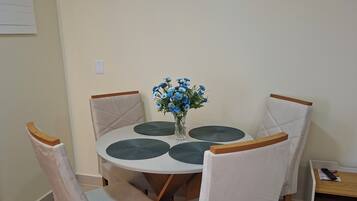 A dining area with a round table, four chairs, and a vase with blue flowers.