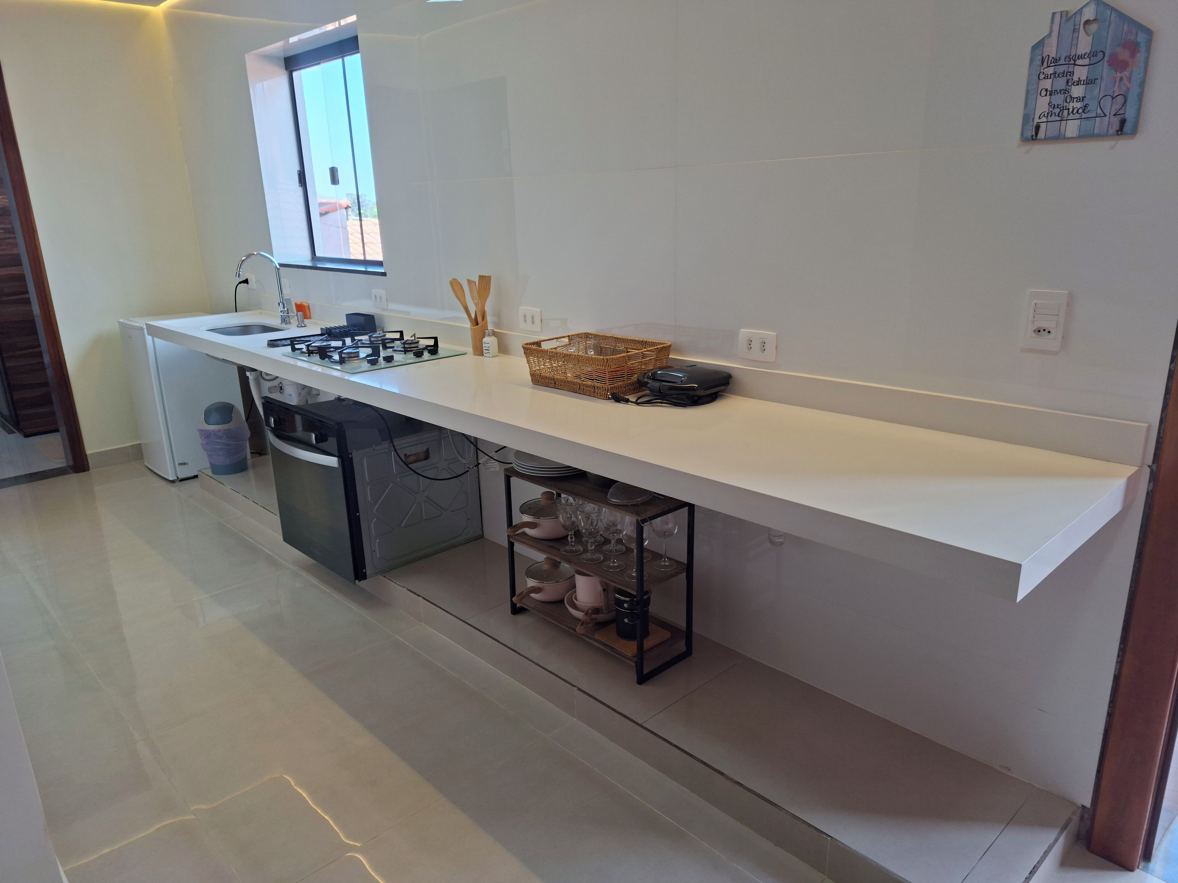 A modern kitchen with a white countertop, a window, and a built-in trash bin.